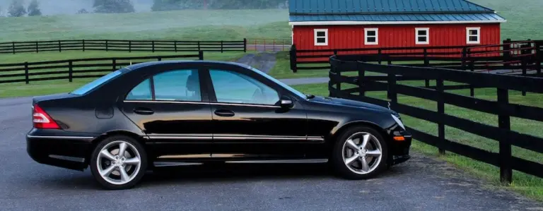 Black sedan parked beside a white ranch fence and a red barn