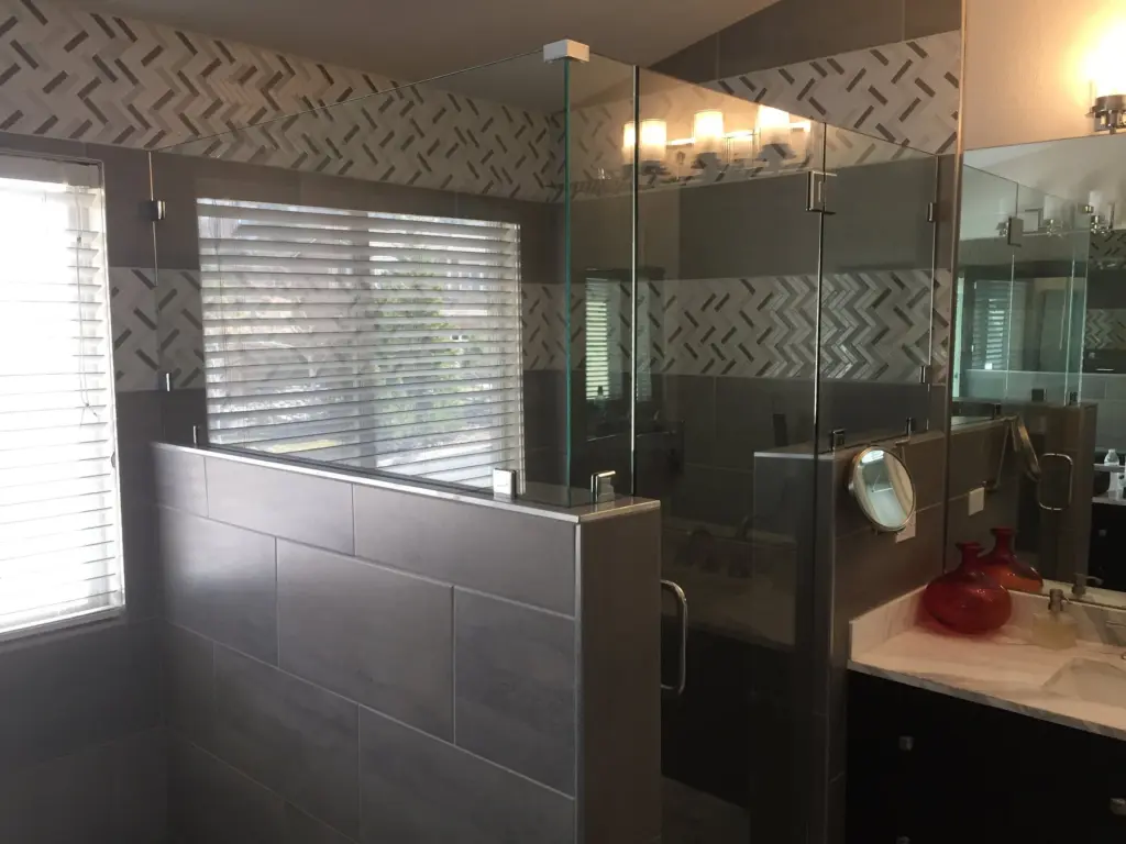 Bathroom with a frameless glass shower enclosure, gray herringbone tile walls and a white subway tile surround