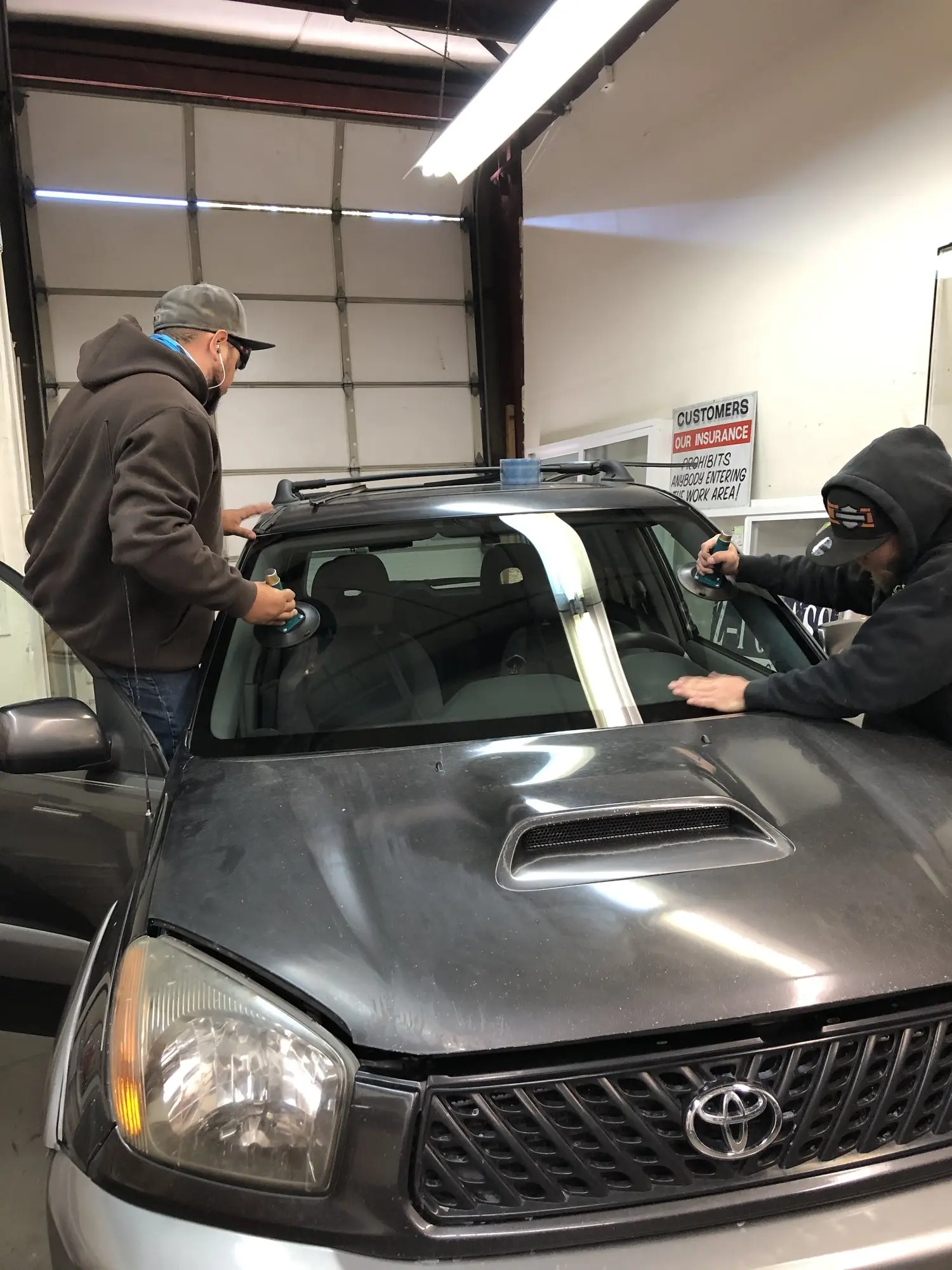 Two Z-1 Glass technicians setting a new windshield on a gray Toyota in the shop